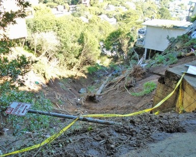 A view looking downhill of the damage from a mudslide in Sausalito, with a wrecked home at the bottom of the hill.