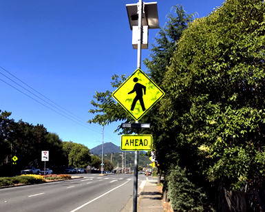 A new pedestrian safety crosswalk beacon installed on a sign adjacent to a busy road.