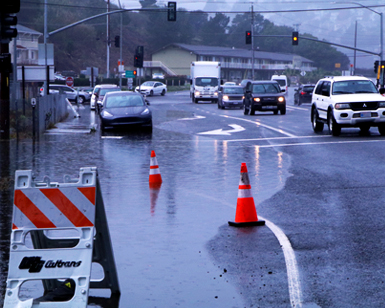A view of flooded roadway and vehicles moving around puddles at the entrance of the Manzanita Park & Ride lot near Sausalito.