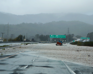 A road-level view of Highway 37 during recent flooding, with a truck stuck in the water in the distance.