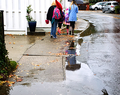 McAllister Avenue is shown with puddles in the gutter overflowing to the sidewalk and children walking to school in the background.