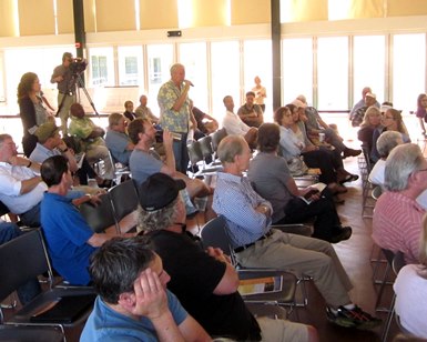 A man speaks with a microphone in front of a group of people attending a flood control meeting.