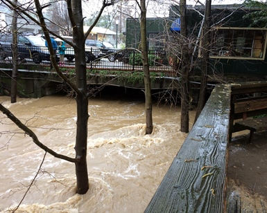 Muddy flood waters in Corte Madera Creek get close to flood level near buildings in downtown San Anselmo.