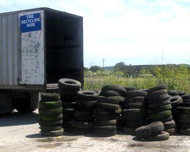 Stacks of old tires sit outside a trailer during recycling event.