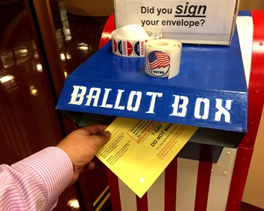 A man's hand holds a voter ballot as he puts it into a ballot box.