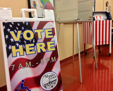 A sign in the Elections Department says "Vote Here" next to a voting booth.