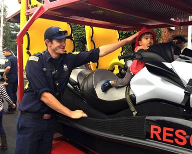 A firefighter smiles has he holds onto a young boy who is sitting on a water rescue vehicle during a community fundraiser