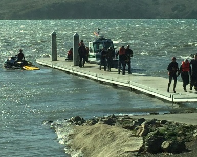 Rescued people walk on a pier toward safety as a single-person watercraft and a larger rescue boat are docked at the end of the pier.