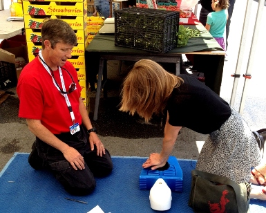 A man on the left watches as a woman practices CPR on a large spongy block.
