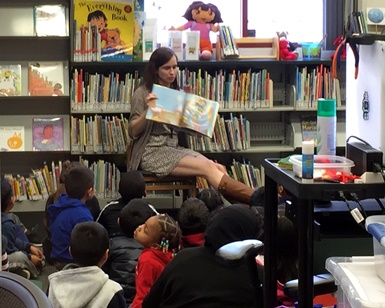 A librarian holds up a book in front of about 10 children during storytime at the Marin City Library.