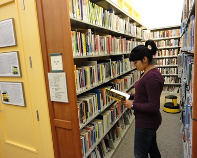 A young girl looks through books while standing in a library