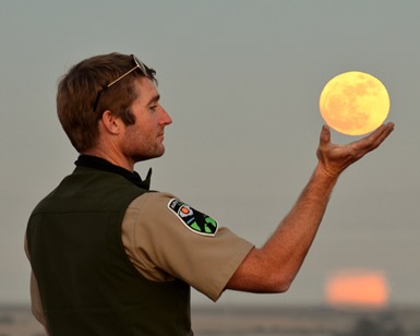 A park ranger holds out his hand and the distant moon appears to be resting in his hand.