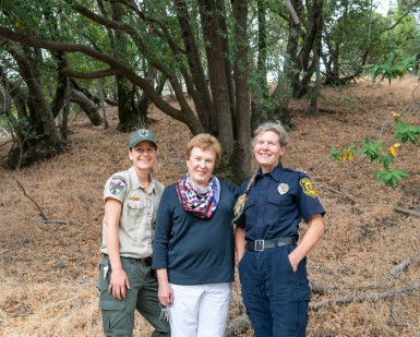 A female park ranger, a female resident and a female firefighter pose and smile in a wooded area of Pacheco Valle.