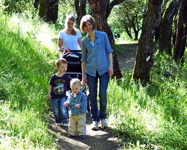 Two moms and two young kids smile as they walk on a trail.