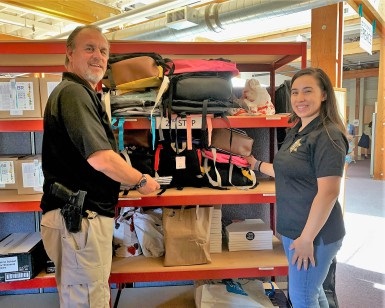 Deputy Probation Officer Mark Messner and Probation Officer Brenda Godoy stand next to shelves with backpacks and other school supplies.