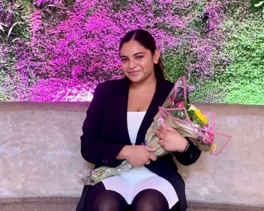 A young woman from the Career Explorers program sits and smiles and holds a bouquet of flowers.