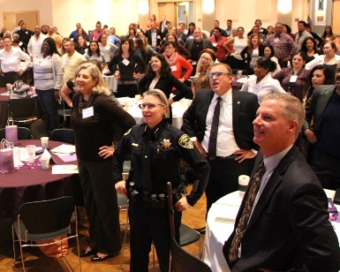 Dozens of people stand up and look toward the state in a ballroom during the 2015 Family Violence Summit