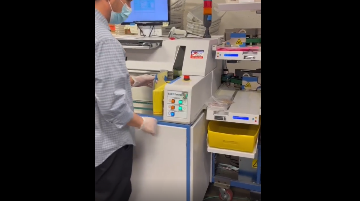 Vote-by-mail ballots running through the ballot sorter machine and staff members removing ballots from return envelopes