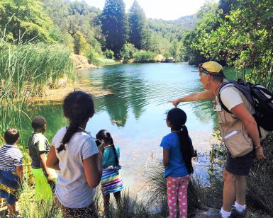 About six kids look out toward Phoenix Lake in Marin County as a female docent points out into the water.