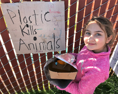 A young girl stands with discarded plastic in her hands next to a sign that says Plastic Kills Animals.