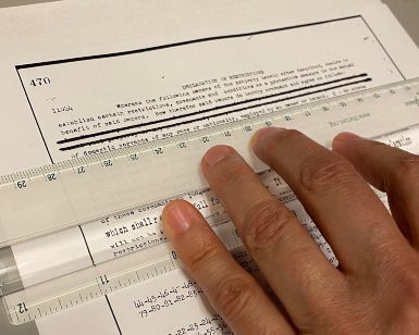 A closeup view of a person's hand holding a ruler while redacting passages on a piece of paper.