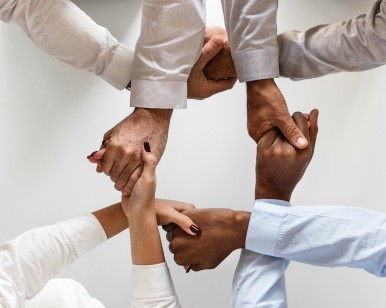 In an overhead view, hands of four people are linked in a circle.