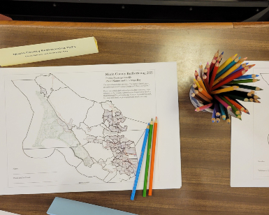 an overhead view of a piece of paper on a table that shows a map of Marin County with a jar of colored pencils off to the right.