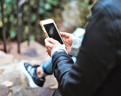 A person sits on an outdoor bench and holds a cell phone.