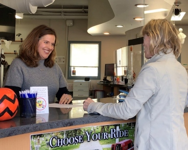 A smiling woman at left is listening to another woman at right with a counter between them.