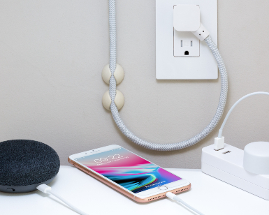 A photo of a smartphone and a small speaker plugged into a wall socket.