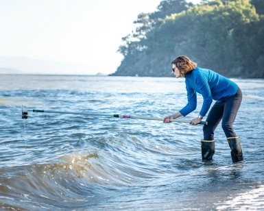 Lorene Jackson of the County's Environmental Health Division uses a pole to scoop water out of the Pacific Ocean for testing.