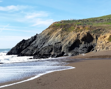 A view of Rodeo Beach in the Marin Headlands, showing sand, water, and a hillside