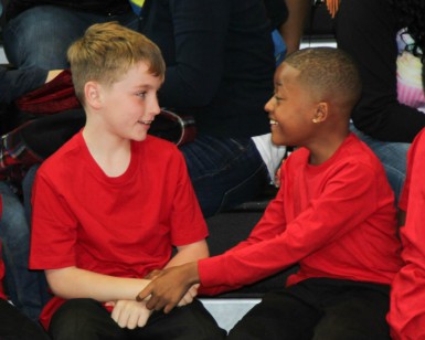 A white boy and an African-American boy shake hands and smile at each other.
