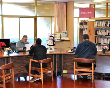A view of the Community Development Agency customer service desk, with two residents sitting in chairs facing away from the camera and an employee talking to one of them.