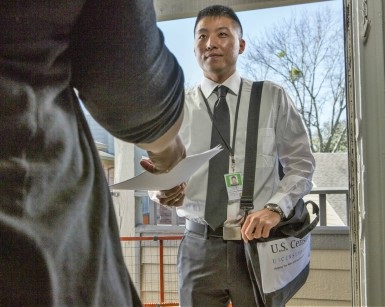 A young man working for the U.S. Census hands over papers to a person at the front door of a home.