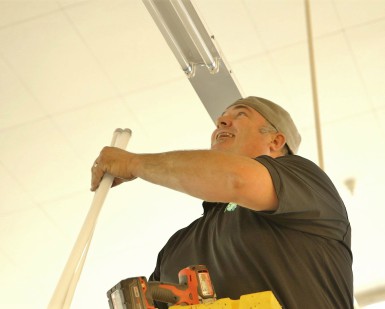 A worker on a ladder installs efficient LED lighting at Fairfax Market.