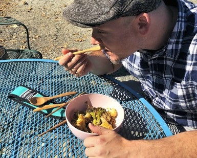 A man sits at a table and eats his lunch with a wooden fork