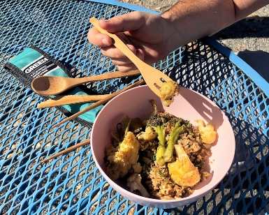 A closeup view of a person's hand using wooden utensils to scoop food out of a bowl during lunchtime.