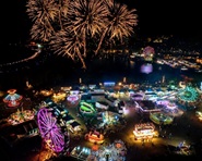 A nighttime aerial drone view of fireworks exploding over the illuminated fairgrounds. 