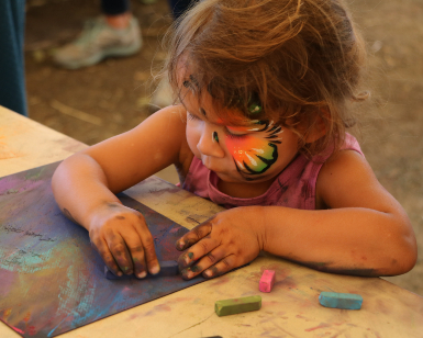 A young girl with a painted face draws with chalk at the Marin County Fair.
