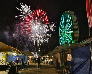 A nighttime view of a fireworks blast in the sky and the ferris wheel with green lights.