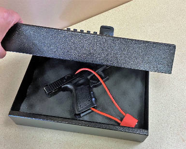 A closeup view of a lunchbox-sized firearm locker with a pistol inside and lock around the pistol. 