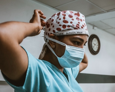 A nurse wearing scrubs ties on a surgical mask.