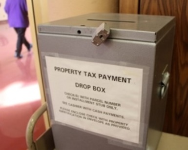 A silver box sitting in a Civic Center office has a sign that says Property Tax Payment Drop Box