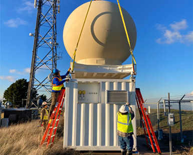 Construction workers install a weather radar apparatus on top of a hill.