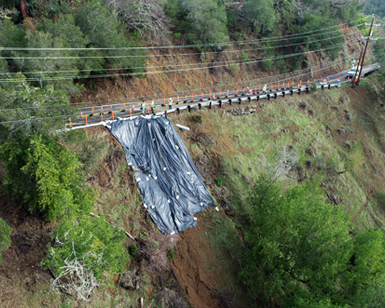 An aerial view of damage to Bolinas Road, with tarp covering ground next to the roadway.