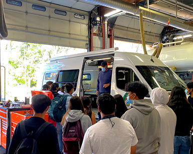 A group of high school students gathered around a van in the county garage listening to a public works employee speak about his job.