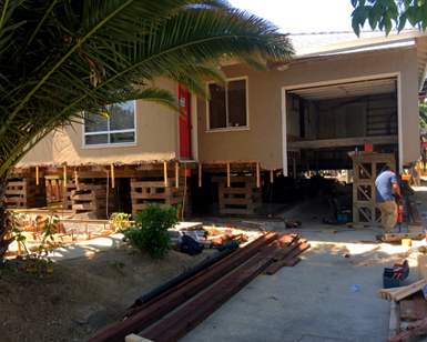 A residential home is shown propped up by wooden struts as workers rebuild a higher foundation.