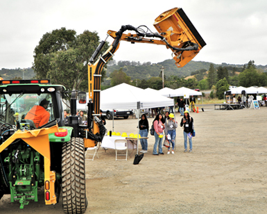 Four teenage girls stand near a piece of heavy construction equipment operated by a Public Works employee