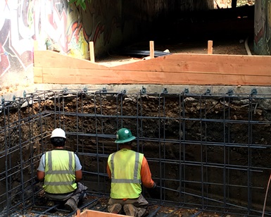 Two construction workers kneel in the dirt as they work on a fish passage project.